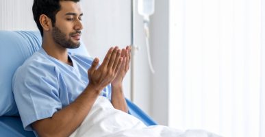 Firefly_A young man is sick, wrapped in a blanket in the hospital room, praying with his hand 414914